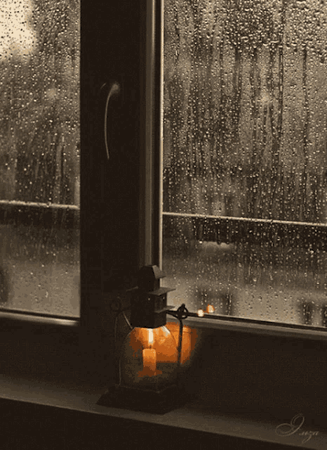 a lantern sits on a window sill in front of a window with rain drops on the glass