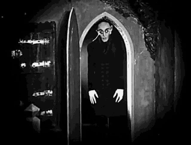 a black and white photo of a vampire standing in an archway .