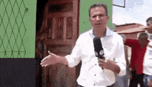 a man in a white shirt is holding a microphone and talking to a group of people .