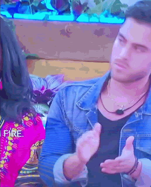 a man in a denim jacket is talking to a woman in a pink shirt that says fire on it
