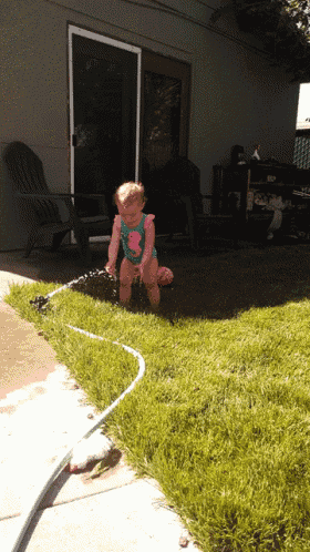 a little girl is playing with a hose in a yard