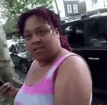 a woman in a pink tank top is standing in front of a black car .