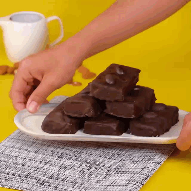 a person is holding a white plate with a stack of chocolate bars on it