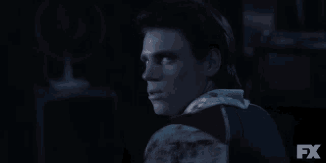a man with blood on his shoulder is looking at the camera in a dark room .