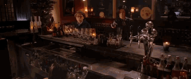 a man in a hat stands behind a bar filled with lots of bottles and glasses
