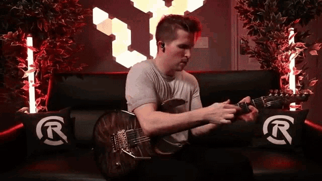 a man sitting on a couch playing a guitar with a r on the pillow