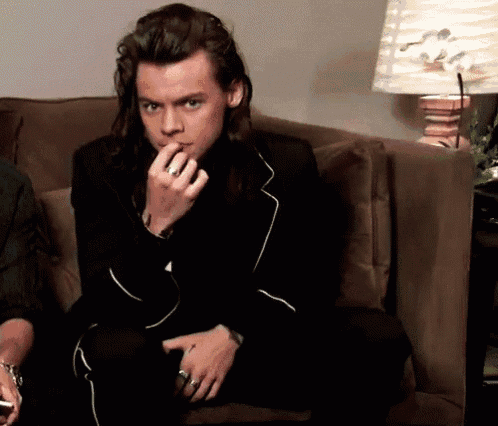 a man with long hair is sitting on a couch with his hand on his mouth