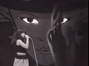 a woman is singing into a microphone in front of a large drawing of a woman 's face .