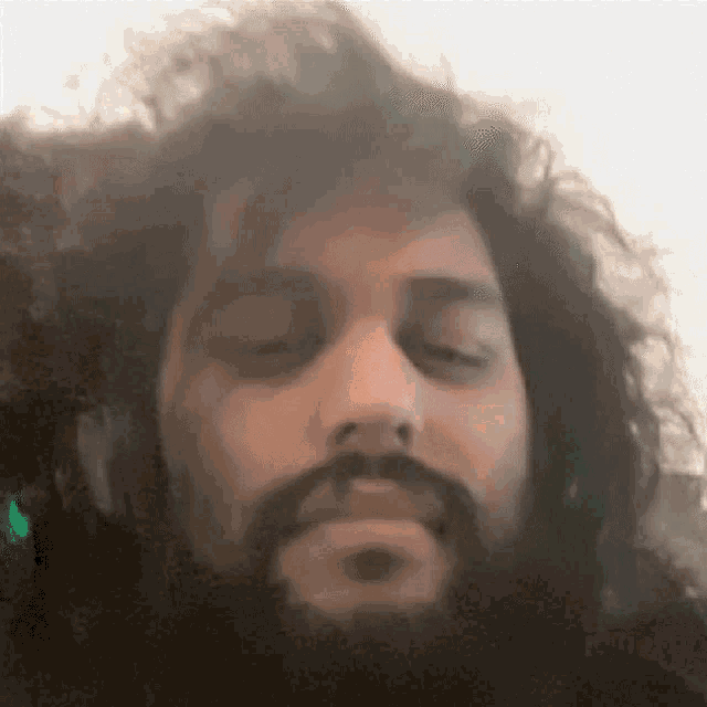 a man with a beard and curly hair is making a funny face with his eyes closed .