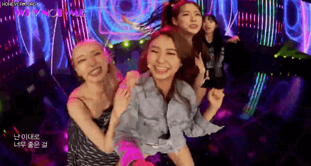 a group of women are dancing on a stage in front of a neon background .
