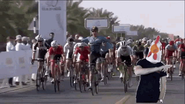 a man wearing a chicken head stands in front of a group of bicycle riders