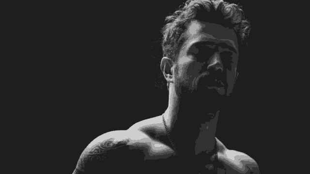 a black and white photo of a shirtless man with tattoos on his arms