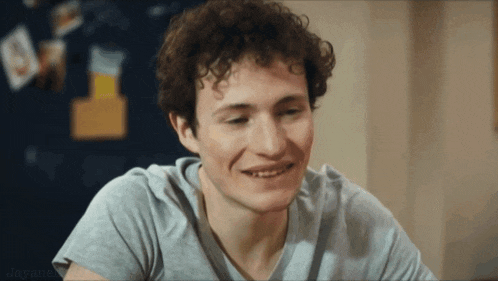 a man with curly hair is smiling and wearing a gray shirt