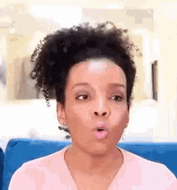 a woman with curly hair is sitting on a blue couch with her mouth open .