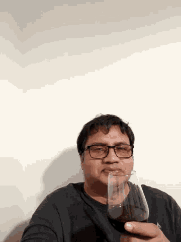 a man wearing glasses is holding a glass in his hand