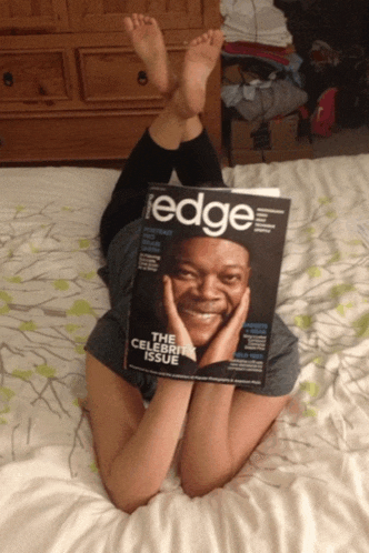 a person laying on a bed holding a magazine called edge