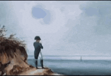 a man is standing on top of a cliff overlooking the ocean looking through binoculars .