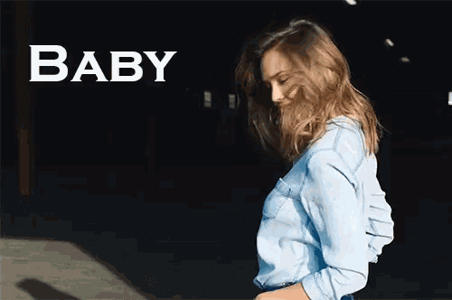 a woman in a denim shirt stands in front of a sign that says baby