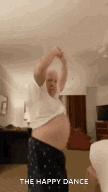 an older man is dancing in a living room with his shirt off and his belly exposed .