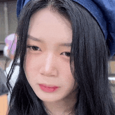 a woman with long black hair wearing a blue hat looks at the camera