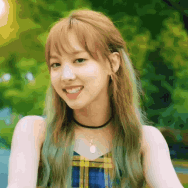 a girl with blonde hair and green hair is smiling and wearing a plaid top and a choker necklace .
