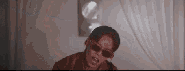 a man wearing sunglasses is sitting on a bed in a dark room .