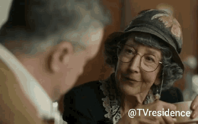 an elderly woman wearing glasses and a hat is talking to a man
