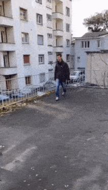 a man in a black jacket is walking down a sidewalk next to a building