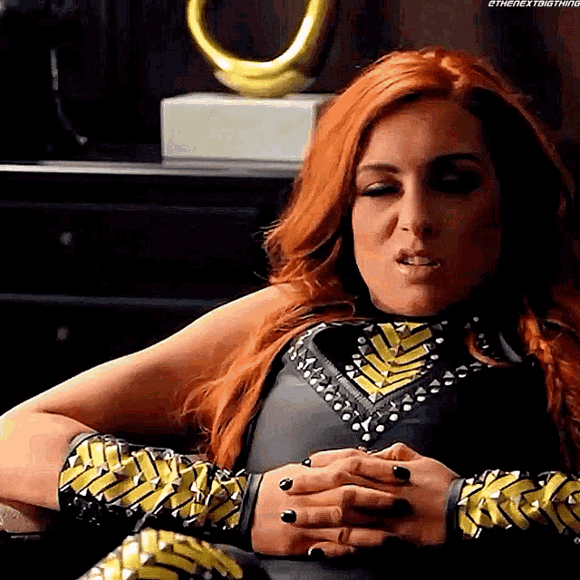 a woman with red hair and black nails is sitting in a chair with her hands folded