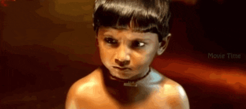 a young boy without a shirt is looking at the camera .