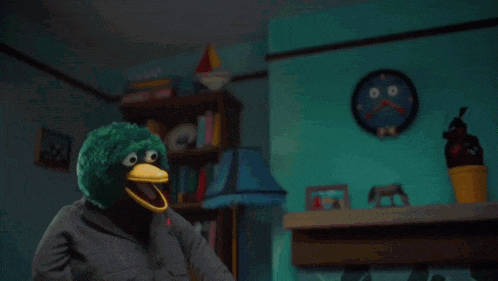 a green stuffed animal with a yellow beak and big eyes is holding a yellow object .