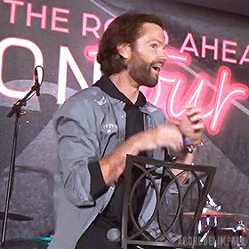 a man is singing into a microphone in front of a sign that says " the road ahead "