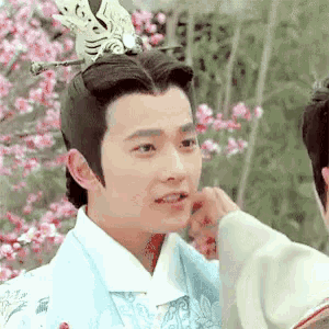 a man in a costume is being touched by another man in front of a cherry blossom tree .