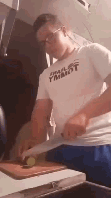 a man is cutting a lime on a cutting board while wearing a small ymmot shirt .