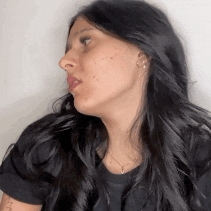 a woman with long black hair is making a funny face while wearing a black shirt and earrings .
