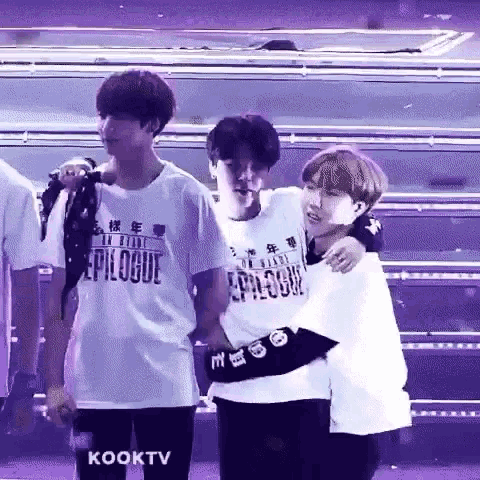 a group of young men are standing next to each other on a stage and hugging each other .