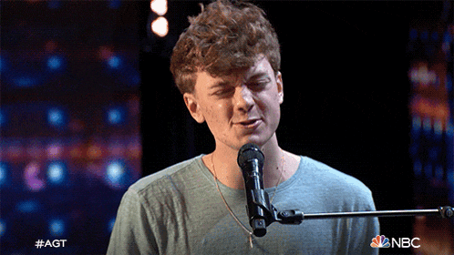 a young man singing into a microphone with nbc written on the bottom