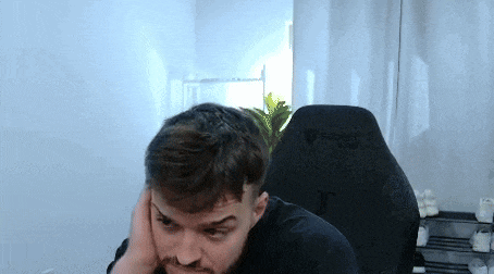 a man with a beard is sitting in a gaming chair and covering his ears .