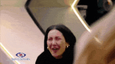 a woman is crying in front of a sign that says ' grande fratello ' on it