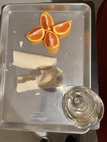 a silver tray with a broken tortilla and sliced oranges sits next to a glass of water