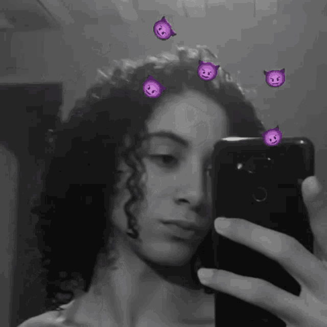 a woman is taking a picture of herself in the mirror with purple devils on her hair .