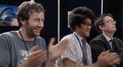 three men are clapping their hands together in a room . one of the men has an afro .