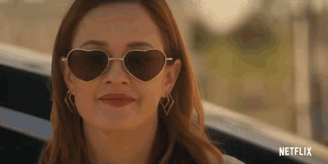 a close up of a woman wearing heart shaped sunglasses with a netflix logo behind her