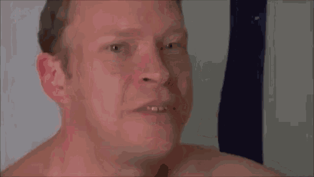 a man without a shirt is making a funny face while looking at the camera .