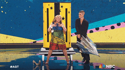 a woman in a colorful dress is being cut in half by a man holding an umbrella in front of a nbc logo