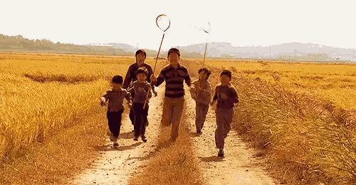 a group of children are running down a dirt road in a field holding hands .