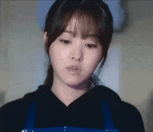 a woman wearing a black hoodie and blue apron looks down