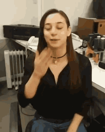 a woman in a black shirt is sitting at a desk with her eyes closed and a choker around her neck .