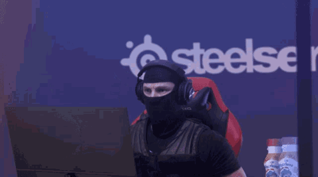 a man in a black mask is pointing a gun at a laptop in front of a steelseries logo