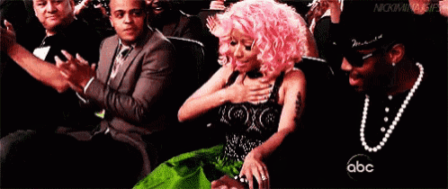 a woman with pink hair is sitting next to a man in a crowd applauding .